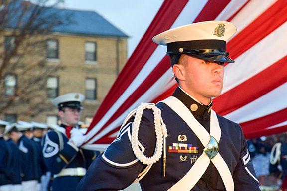 一名军校学员站在一面美国国旗前.